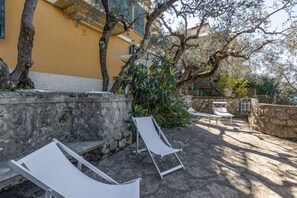 A courtyard with two white lounge chairs, a stone wall, and a yellow building in the background.