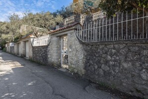 A stone wall with a metal gate, a paved road, and trees in the background.