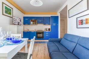 A modern kitchen with blue cabinets, a dining table with blue placemats, and a blue sofa.