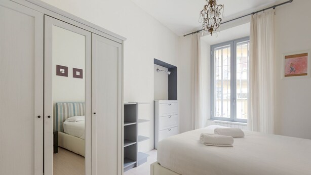 A bedroom with a bed, a wardrobe, a mirror, a window, and a chandelier.