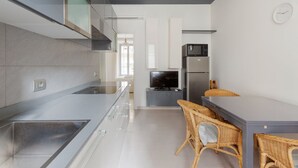 A modern kitchen with a stainless steel range hood, a built-in oven, and a microwave. There is a dining area with wicker chairs and a flat-screen TV.