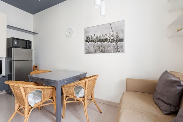 A modern kitchen with a refrigerator, microwave, and dining table with wicker chairs.