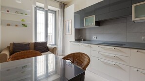 A modern kitchen with white cabinets, a black countertop, and a dining area with a glass table and wicker chairs.