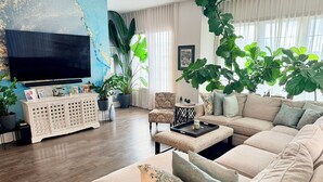 A living room with a sofa, coffee table, and a TV. There are potted plants and a cabinet with photos. - Spacious 2 BR Urban Oasis at Castleberry Station in downtown Atlanta (Atlanta)
