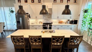 A modern kitchen with white cabinets, a large island with bar stools, pendant lighting, and a refrigerator. - Spacious 2 BR Urban Oasis at Castleberry Station in downtown Atlanta (Atlanta)