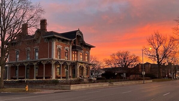 Un bâtiment historique en briques, doté d’un porche, qui ressemble probablement à un hôtel, photographié au coucher du soleil.
