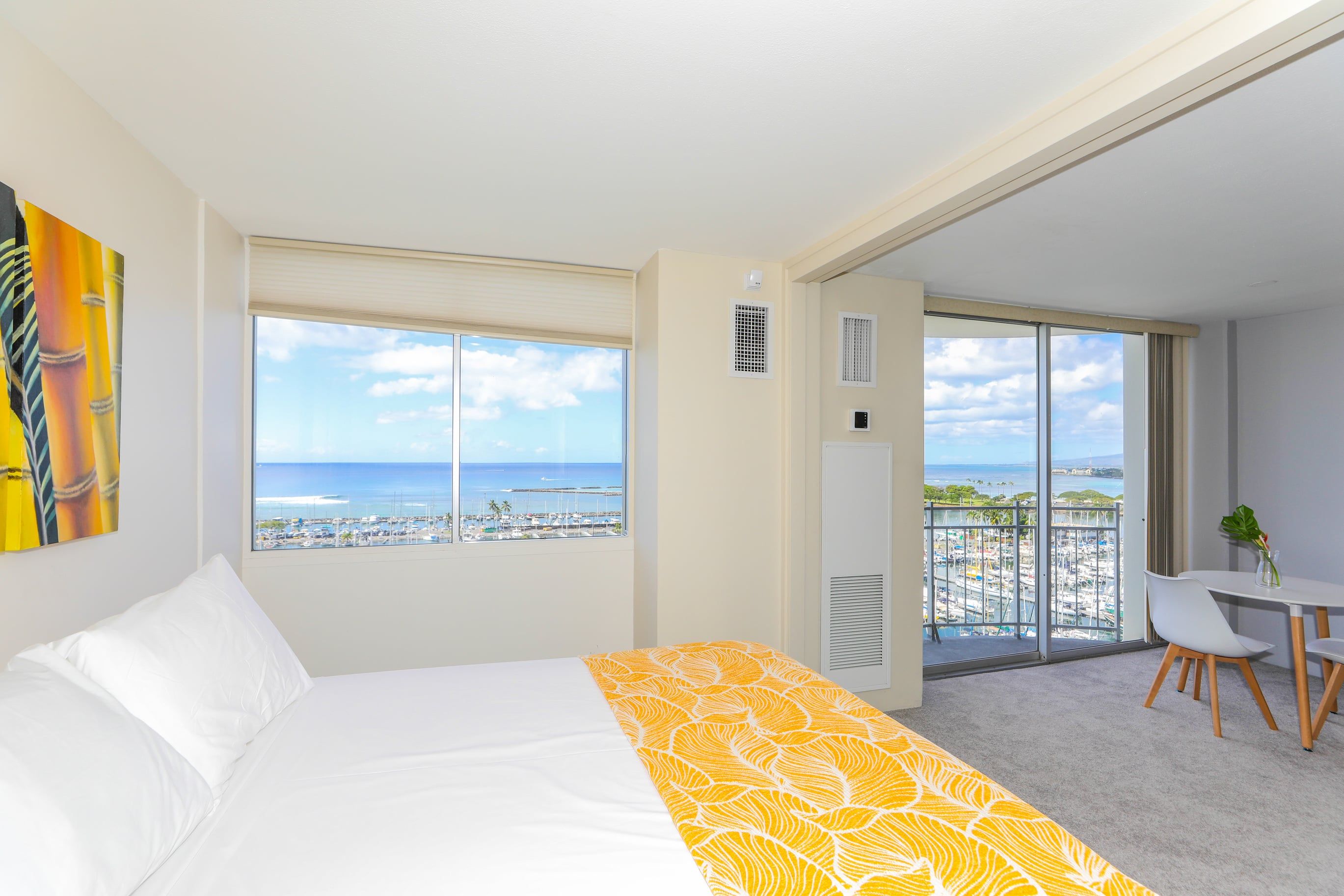 Habitación de hotel con una cama, vistas al puerto deportivo y un balcón con mesa y sillas.
