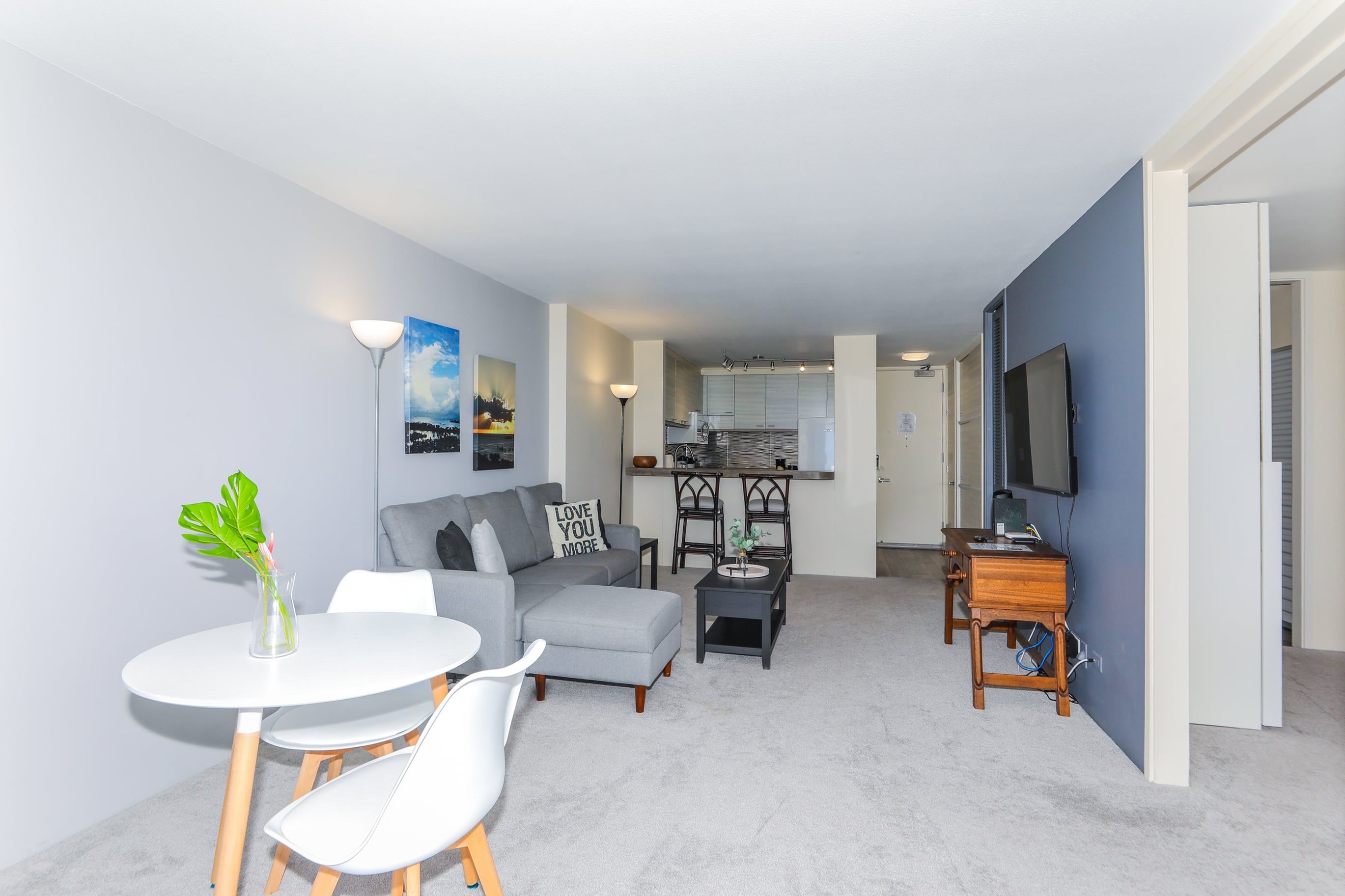En moderne stue med en grå sofa, et hvidt spisebord og et køkken i baggrunden.