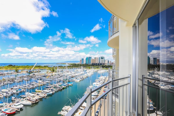 A marina with numerous boats docked, a city skyline in the background, and a clear blue sky.