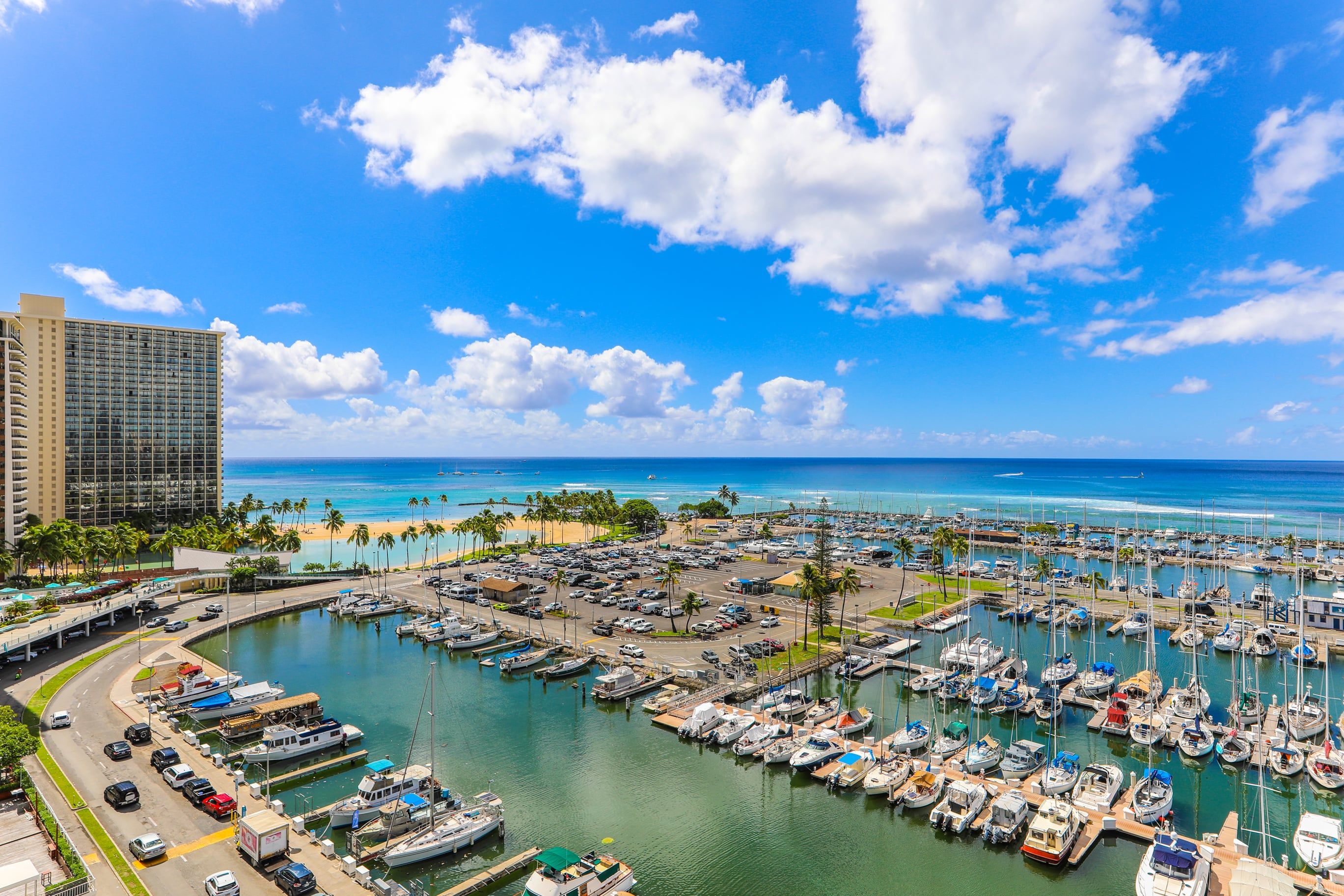 A marina with boats docked, a beach, and a tall building in the background.