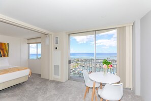 A hotel room with a bed, a dining table with chairs, a view of the marina, and a balcony with a view of the ocean.