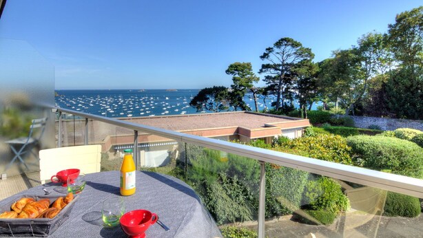 Een balkon met een ontbijtje, met uitzicht op een jachthaven met boten en een heldere blauwe lucht.