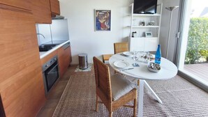 Een compacte keuken met moderne apparatuur, een eethoek met een ronde tafel en stoelen, en een groot raam met uitzicht op groen.
