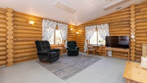 Ein Blockhaushaus-Interieur mit einer Couch, zwei Sesseln, einem Fernseher und einem Schreibtisch.