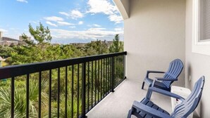 Un balcon avec deux chaises, une vue sur la verdure et les bâtiments, et un ciel dégagé.