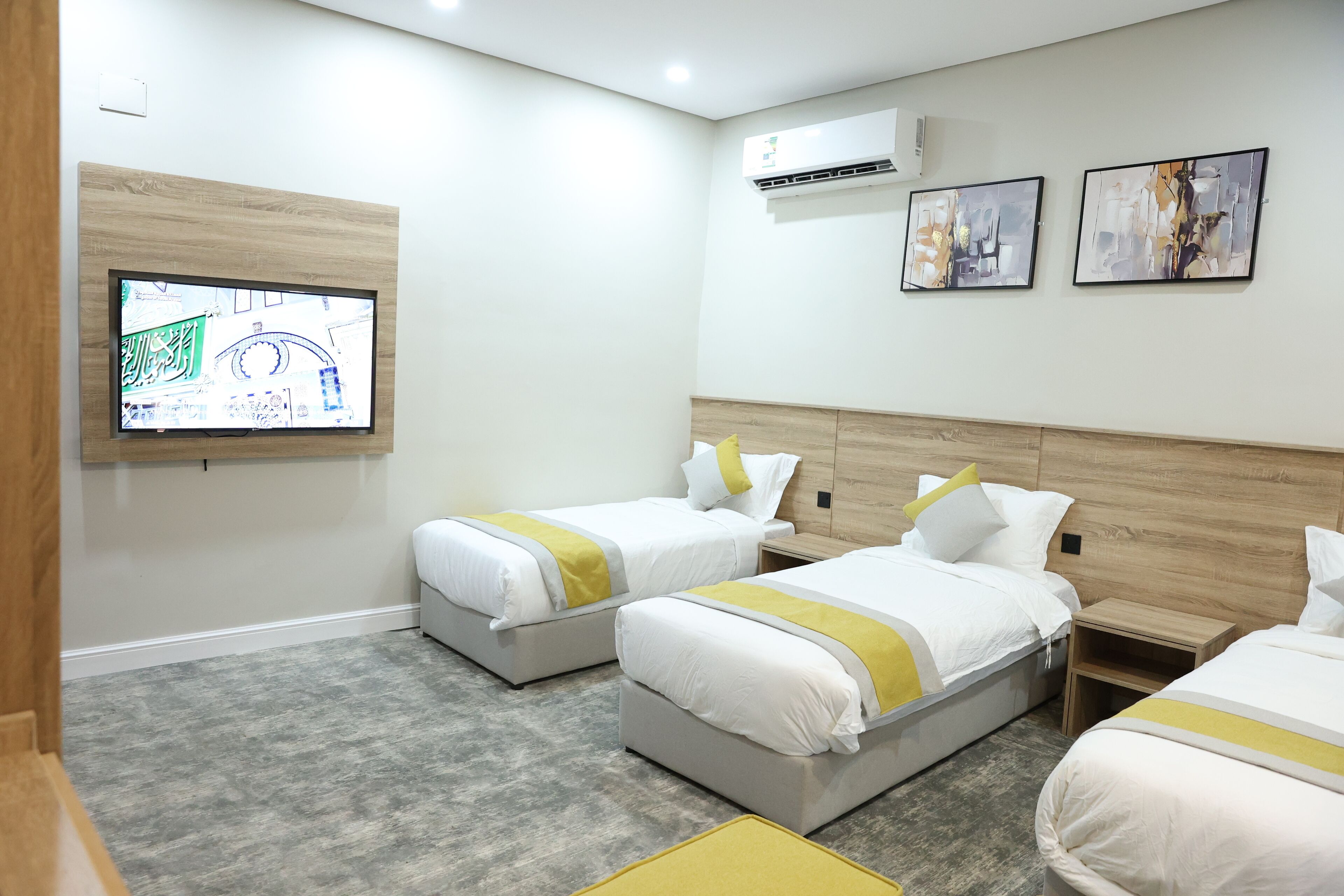 Een hotelkamer met drie bedden, een aan de muur bevestigde televisie en twee ingelijste kunstwerken.