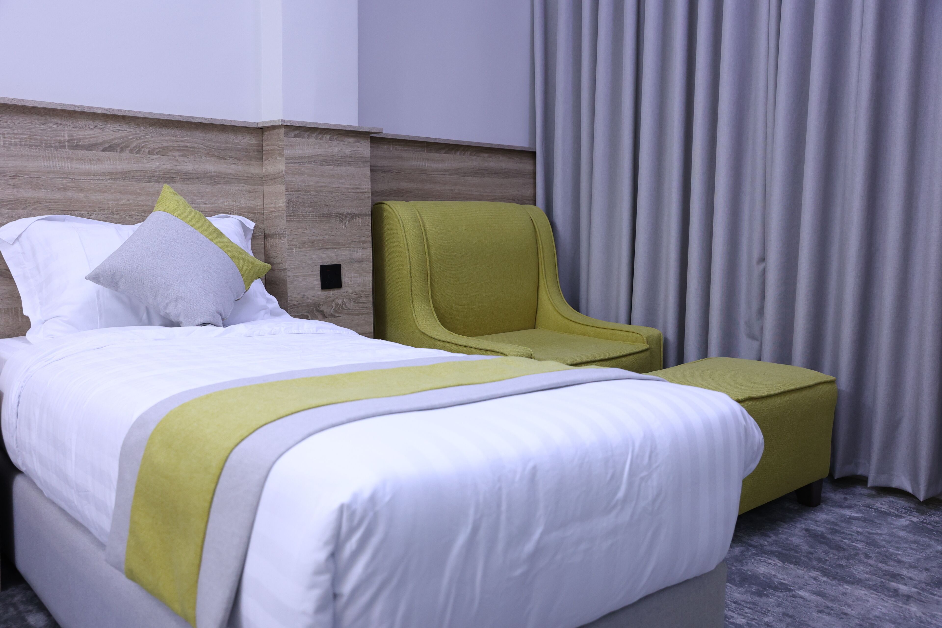 A hotel room with a bed, a green armchair, and a grey ottoman.
