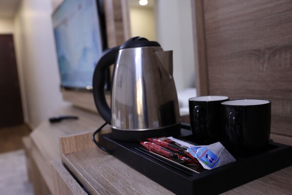 Una estación de café con una tetera, dos tazas negras y un sobre de leche condensada.