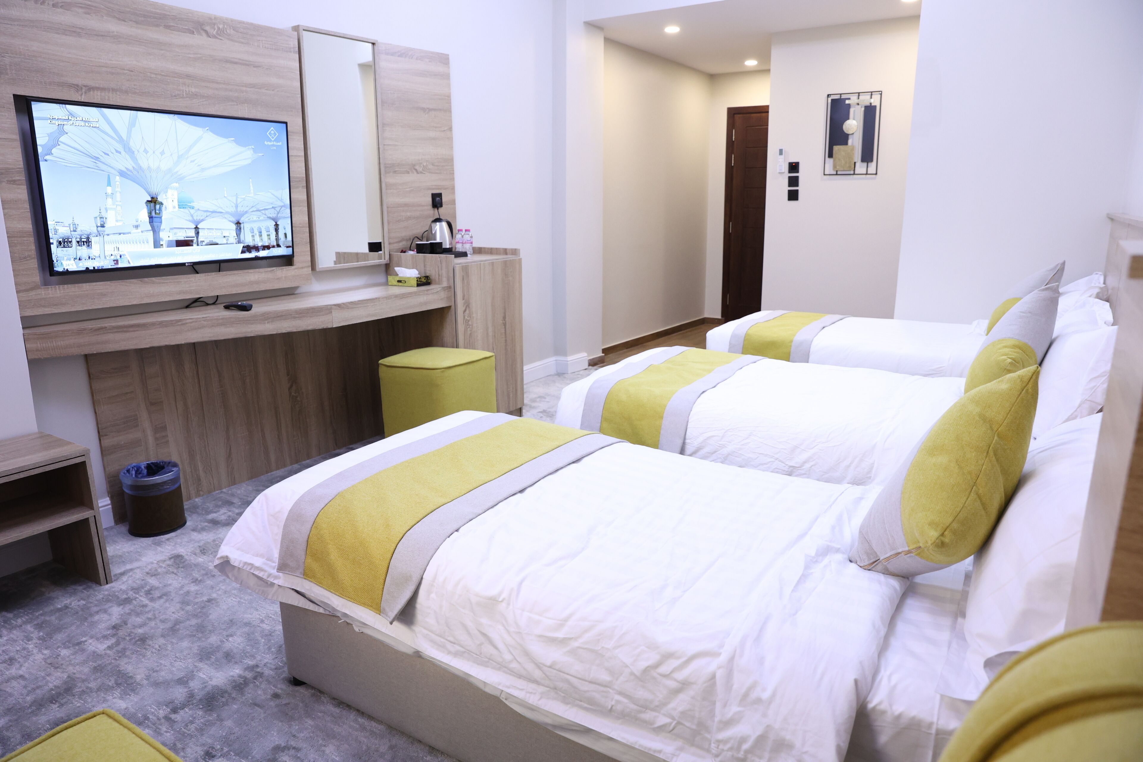 Habitación de hotel con dos camas, un televisor montado en la pared, un escritorio con una silla y un cubo de basura.