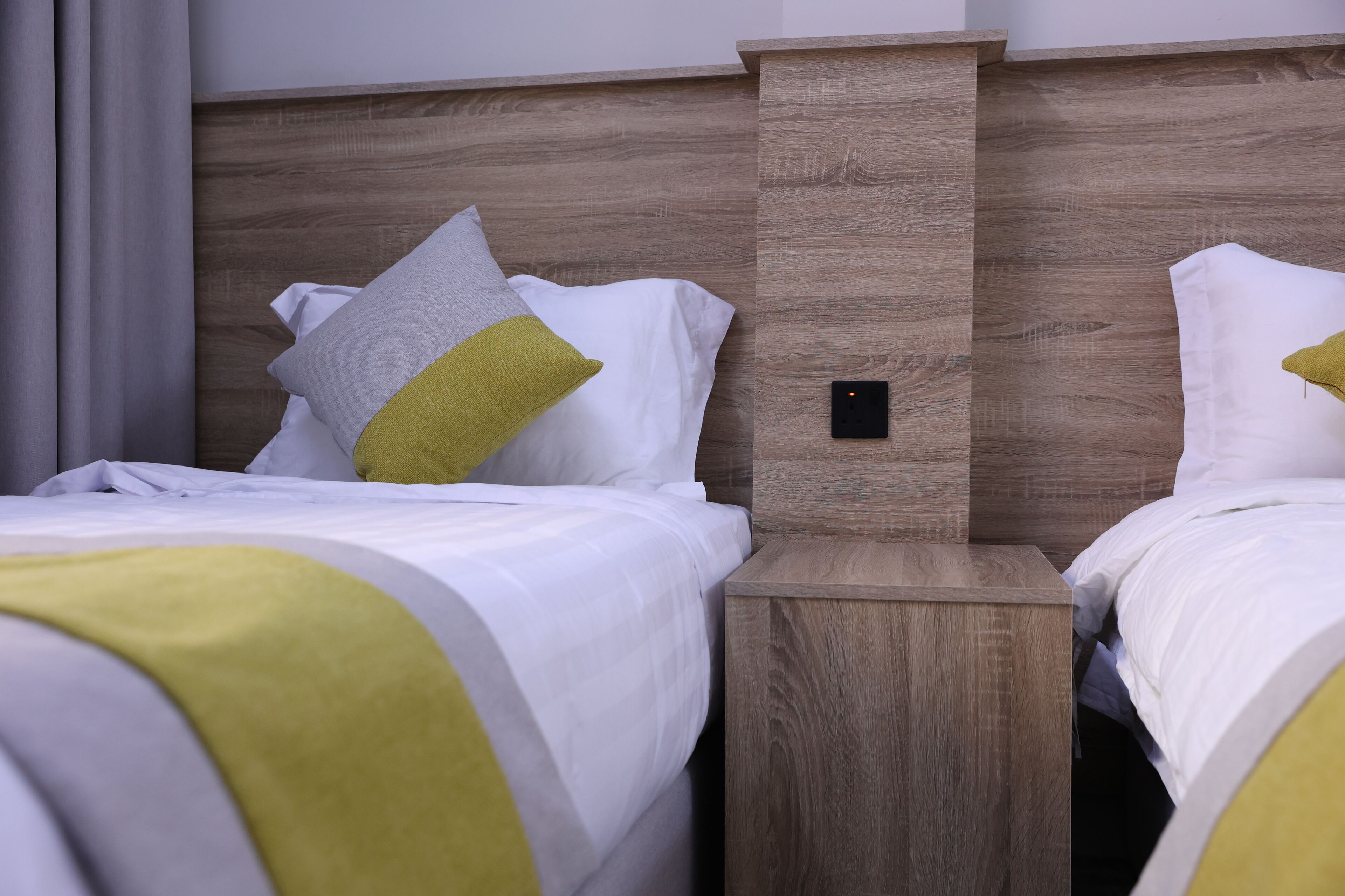 Een hotelkamer met twee bedden, elk voorzien van witte beddengoed en een groen kussen. Er is een houten hoofdbord en een nachtkastje tussen de bedden.