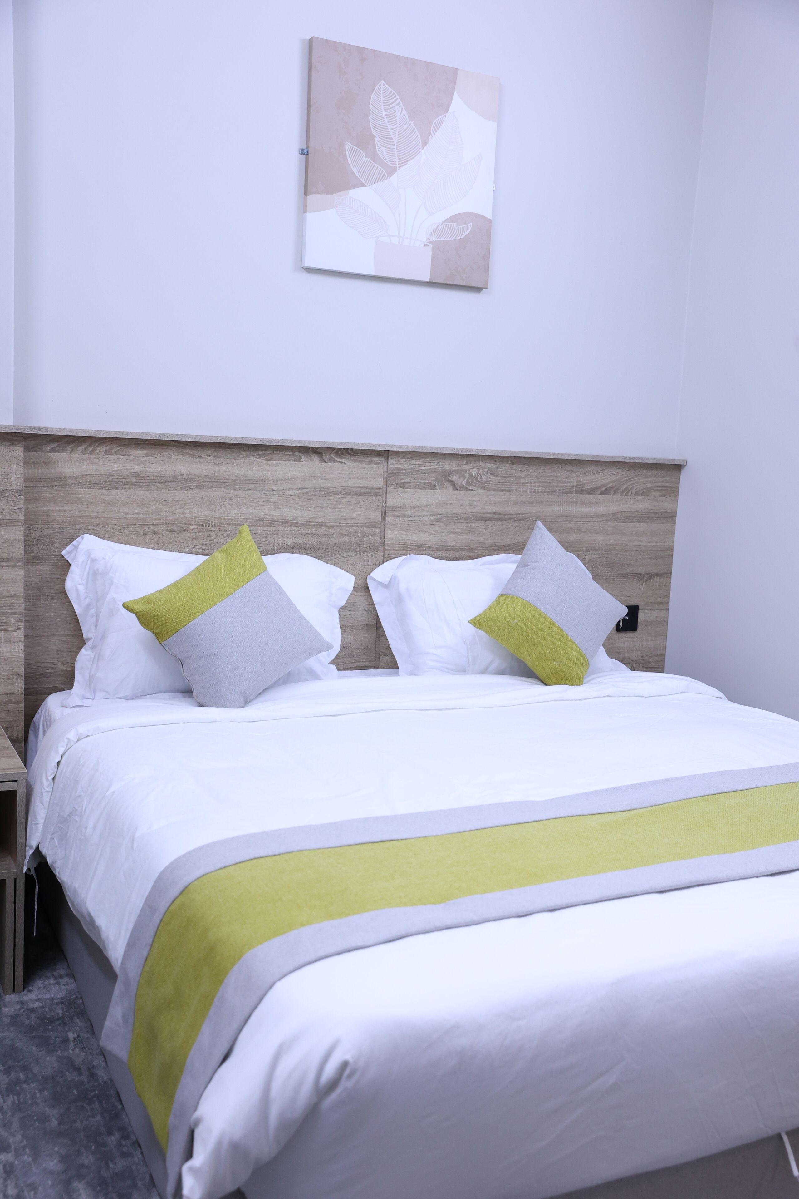 Una cama bien hecha con ropa blanca y detalles verdes, un cabecero de madera y una obra de arte colgada en la pared.