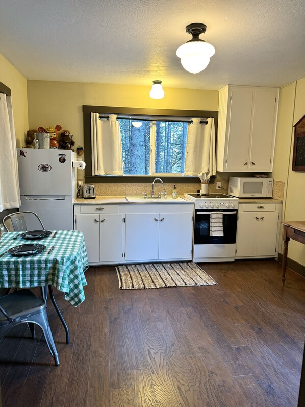 A compact kitchen with white cabinets, a microwave, a refrigerator, and a dining area with a checkered tablecloth.