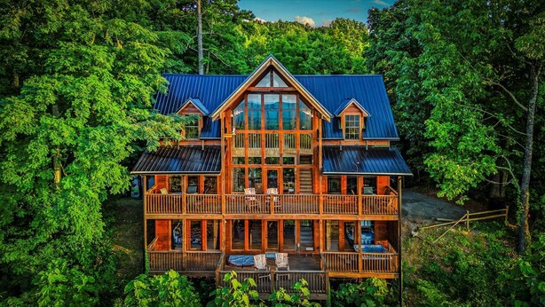 Une grande cabane en bois à deux étages, dotée d’un balcon et d’une terrasse, entourée d’une forêt dense.