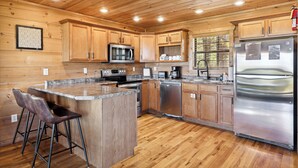 Une cuisine rustique, située dans une cabane en bois, avec un îlot central, des tabourets de bar, des appareils en acier inoxydable et des armoires en bois.