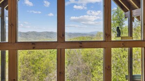 Une cabane en bois dotée de grandes fenêtres qui offrent une vue sur une chaîne de montagnes boisée.