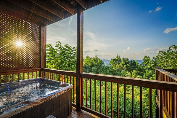 Una terraza de madera con un jacuzzi y vistas a un paisaje boscoso.