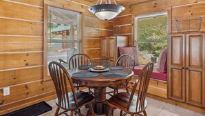 A wooden cabin interior with a dining table surrounded by chairs, a hanging light fixture, and a window with blinds. - The "Lost Horse" Cabin - Secluded - Pet-Friendly - One Level - Massive Yard (Sevierville)