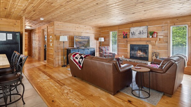 A cozy log cabin interior with a fireplace, leather sofas, a dining area, and wooden walls. - The "Lost Horse" Cabin - Secluded - Pet-Friendly - One Level - Massive Yard (Sevierville)
