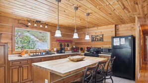 A wooden cabin kitchen with a large island, pendant lights, and a refrigerator. - The "Lost Horse" Cabin - Secluded - Pet-Friendly - One Level - Massive Yard (Sevierville)
