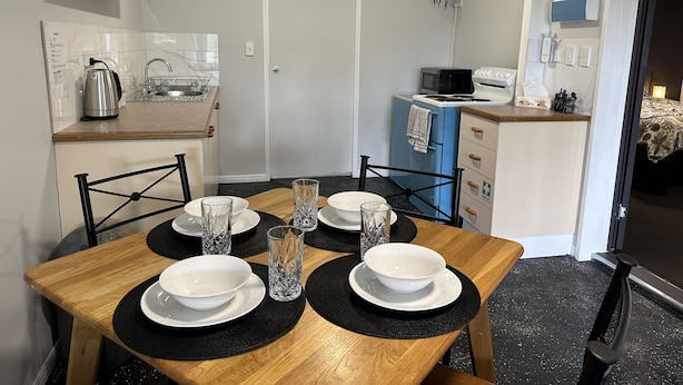 A compact kitchen with a microwave, stove, and sink. There is a dining table with black placemats and white bowls.
