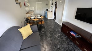 A compact living space with a sofa, a dining table with chairs, a kitchen area, and a television.
