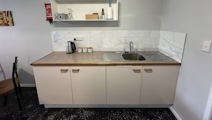 A compact kitchen with a sink, a kettle, and a shelf above the countertop.