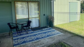 A covered patio area with a table and chairs, a patterned rug, and a green fence.