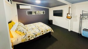 A bedroom with a bed, a mirror, a TV, a guitar, and a speaker.
