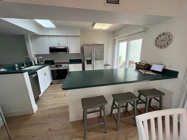 Una cocina moderna con gabinetes blancos, encimera verde y una isla integrada con taburetes.