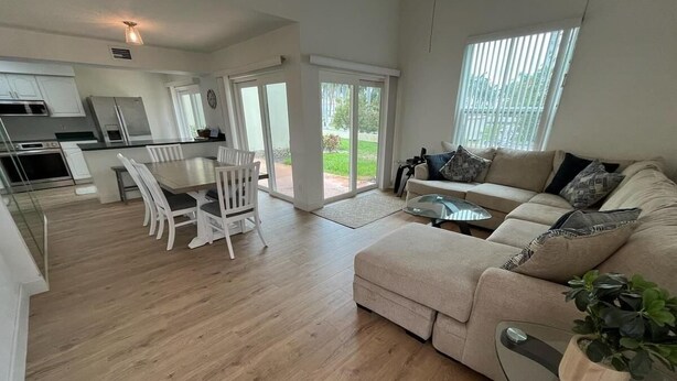 Una sala de estar moderna con un sofá color beige, una mesa de centro de vidrio y un comedor con sillas blancas.