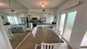 Una cocina moderna con armarios blancos, una isla grande y un comedor con una mesa larga y sillas blancas.