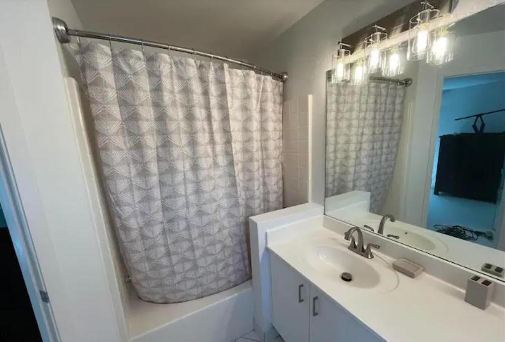 A bathroom with a shower curtain, a sink, a mirror, and a towel rack.