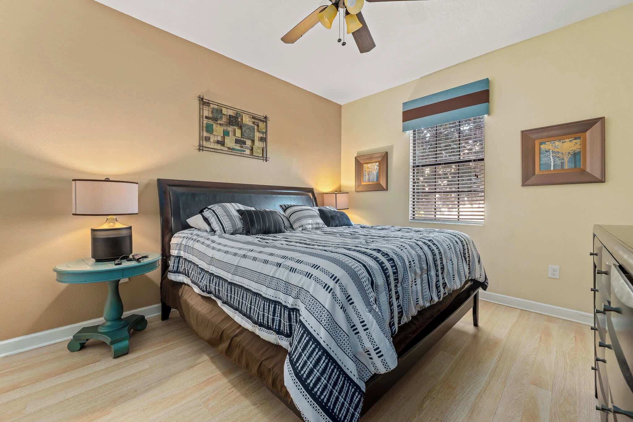 A bedroom with a bed, two bedside lamps, a ceiling fan, and a window with blinds.