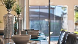 Een eettafel met teal placemats, witte borden en een glazen vaas met groene planten.