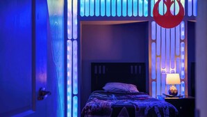 Een slaapkamer met een bed, een nachtkastje met een lamp en een decoratief wandpaneel.