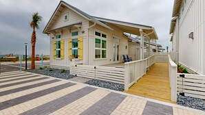 A beachfront building with a wooden deck, a covered walkway, and a palm tree. - Resort Style Pools, Golf Cart Boardwalk to the Beach (Port Aransas)