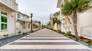 A corridor lined with palm trees and a checkered floor pattern, leading to a building with balconies and windows. - Resort Style Pools, Golf Cart Boardwalk to the Beach (Port Aransas)