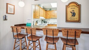 Une cuisine avec des meubles de rangement en bois, un coin bar avec des tabourets en bois et un panneau affichant les règles de la maison, encadré et accroché au mur.