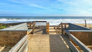 Une promenade en bois mène à des zones aménagées sur la plage, offrant une vue sur l’océan.