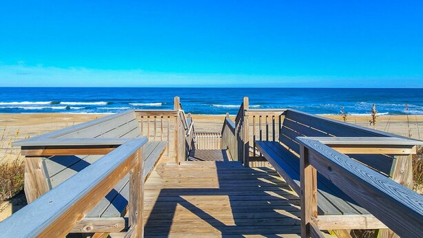 Une promenade en bois menant à la plage, d’où l’on a une vue dégagée sur l’océan.